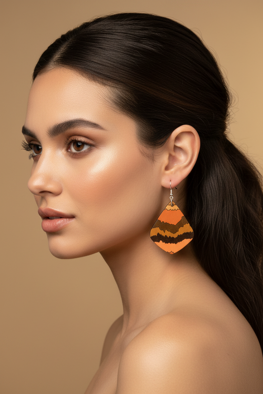 Pair of teardrop-shaped earrings with orange, brown, and black pattern on a beige fabric background.